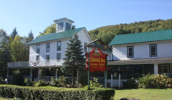 white colonial inn with green roofs and red sign
