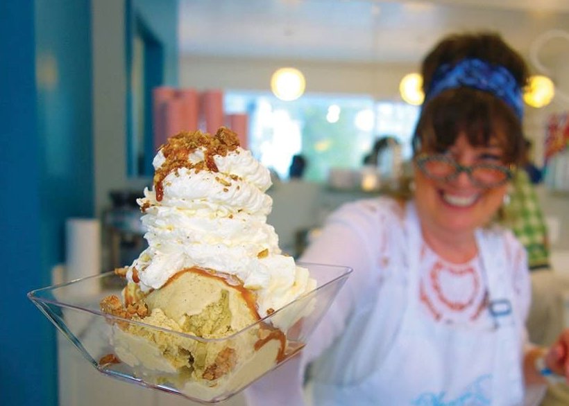 lady offering a triple scoop of pistachio ice cream topped with whipped cream
