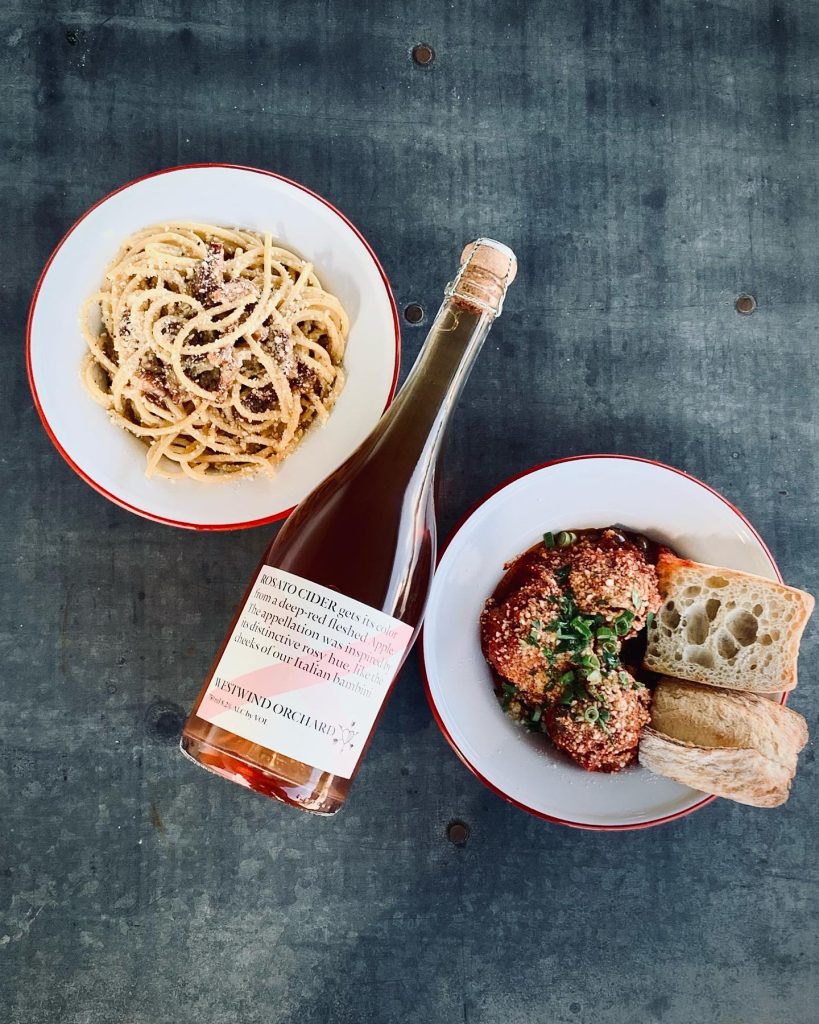 plates of pasta and meatballs and a bottle of rosato cider