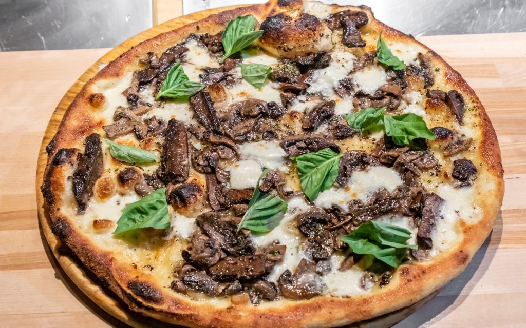 pizza prepared with woodburning oven and garnished with mushrooms, mozzarella and basil