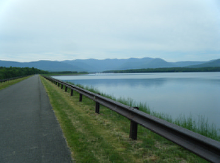 paved road beside a river with hills in the background