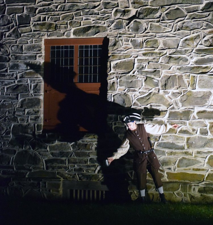 man in colonial costume at night with shadow cast on stone wall