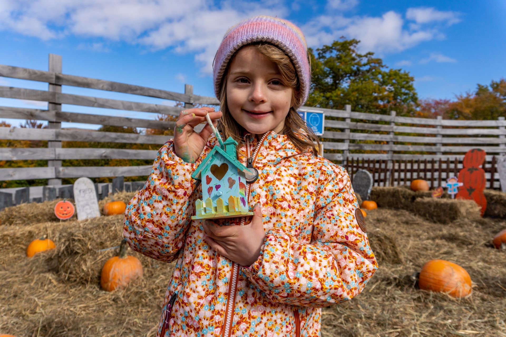 girl holds a handmade birdhouse while standing in pumpkin patch