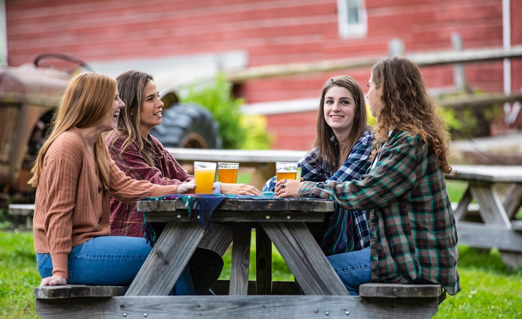 four ladies in fall clothing sitting at a picnic bench drinking beer.