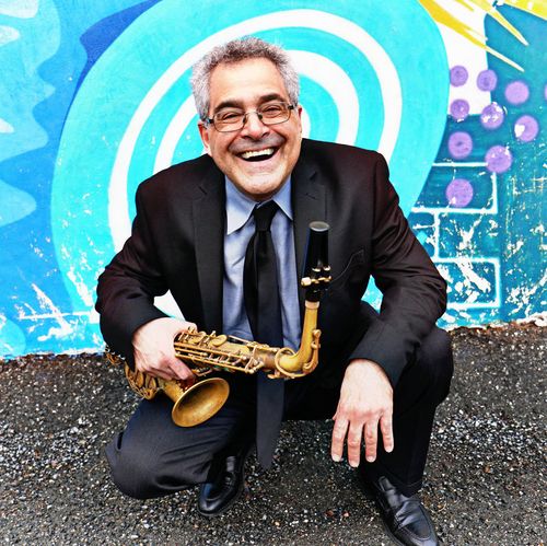 Ed Palermo posing in front of a wall mural with his saxophone