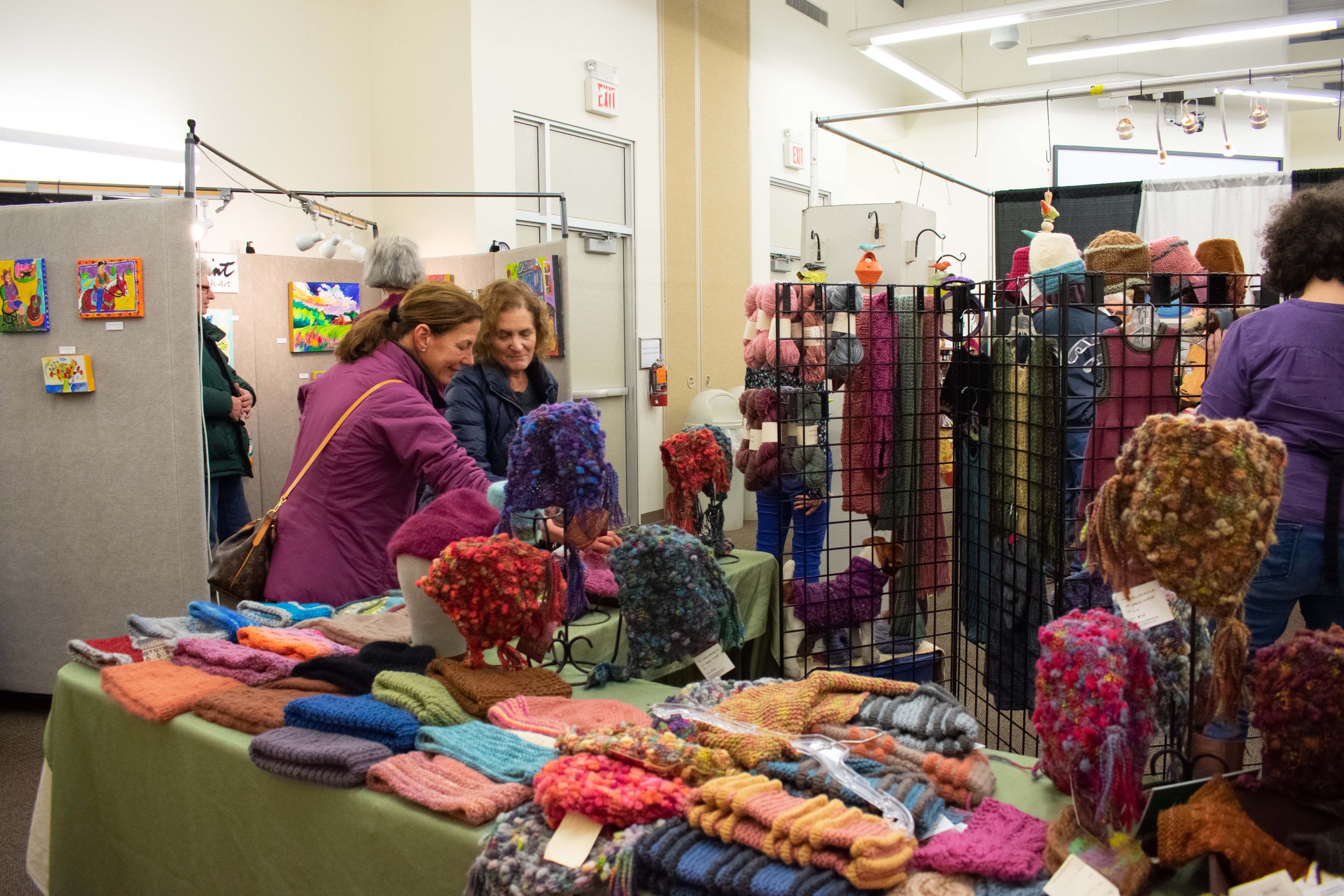 women browsing displays of handmade scarves and hats for sale