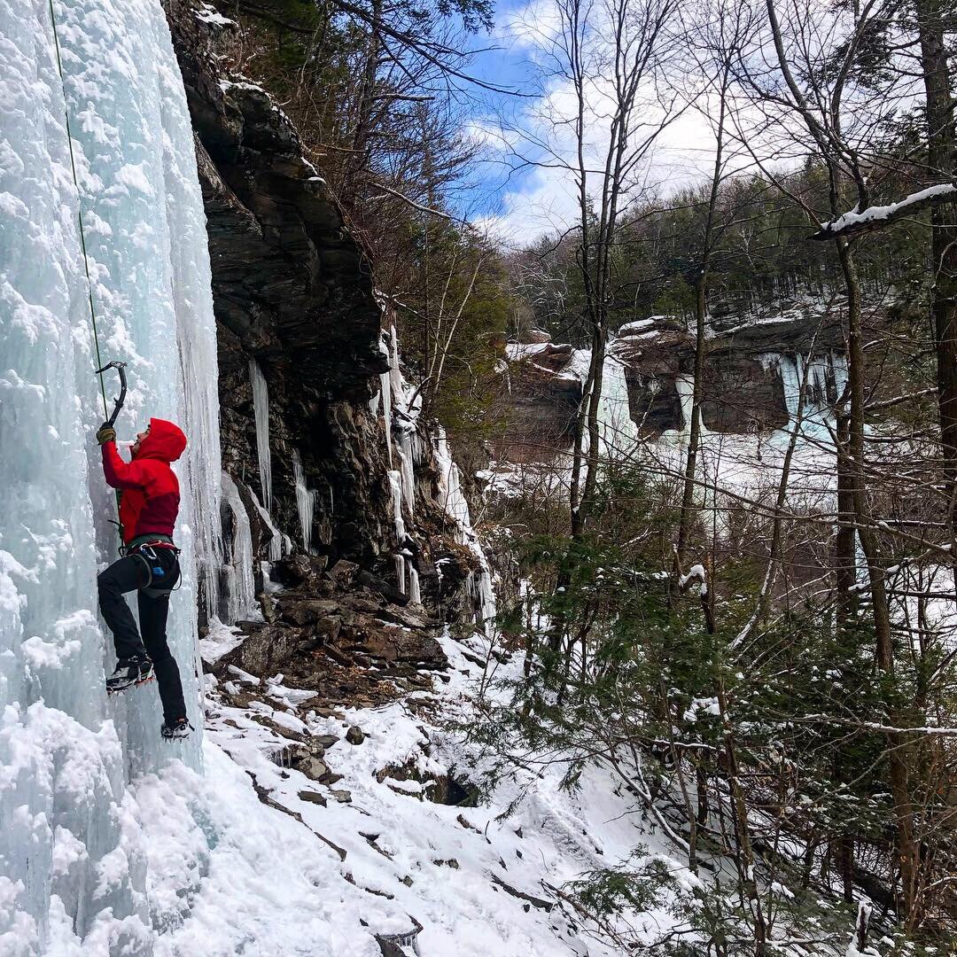 man in red winter coat climbing an ice wall