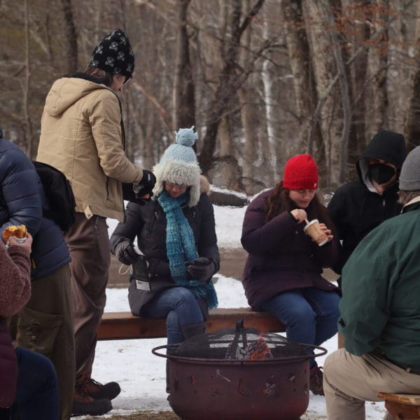 group of people in winter coats around a firepit enjoying hot chocolate