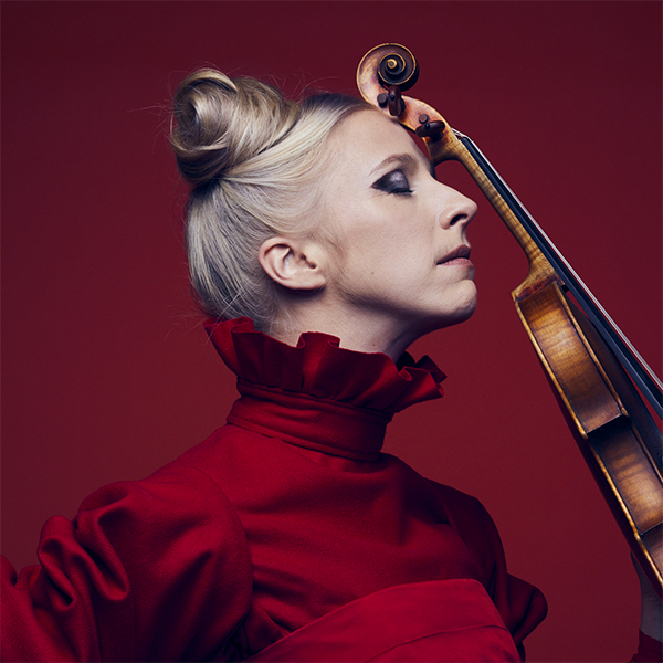 woman in high-neck red top leaning her violin against her forehead