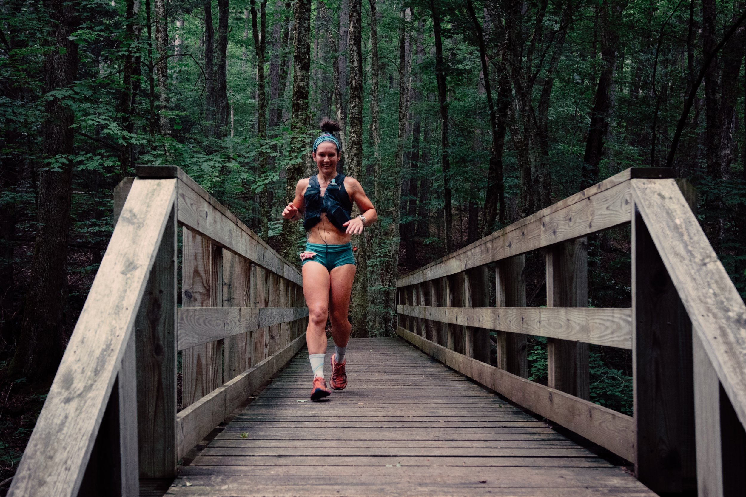 woman in weighted vest running across wooden bridge in forest