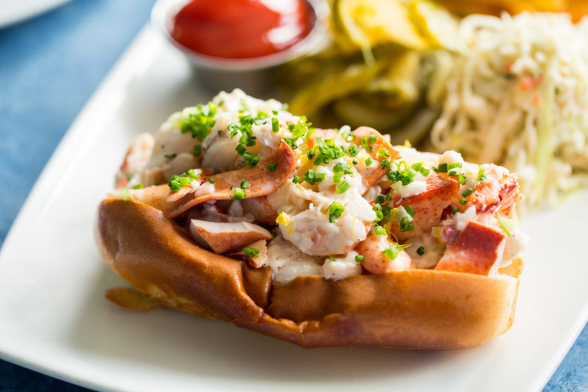 Lobster roll on a plate with other food blurred in the background