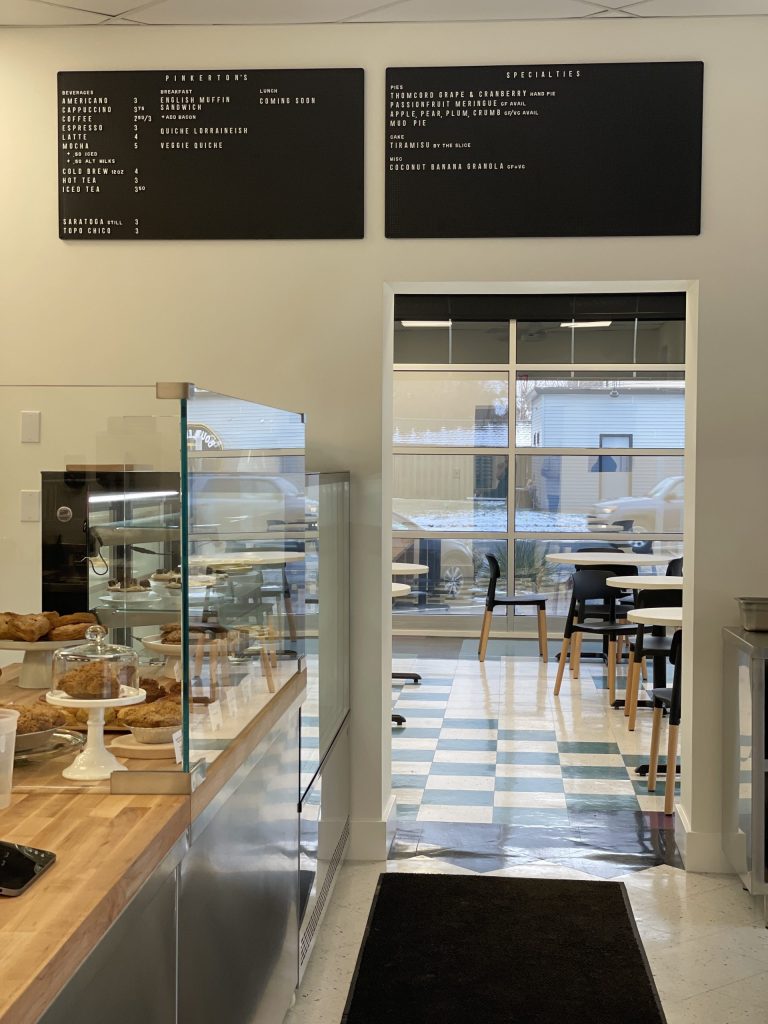 Bright café interior with pastry display case, black menu boards on the wall, and seating by large front windows.