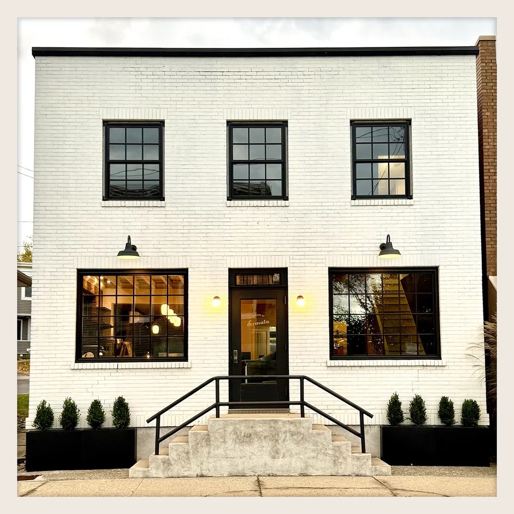 Front entrance of Fermata Cafe & Roastery, a white brick building with large windows and stairway planters.